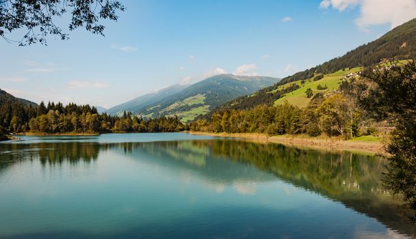 lake panorama on the alps, still water reflects the mountains and green trees