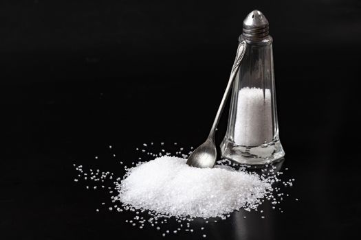 White Salt With Glass Shaker and Silver Spoon Isolated on Blck Background