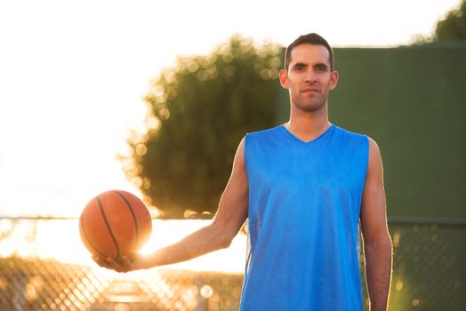 Athlete man holding basketball ball standing on playground at sunset