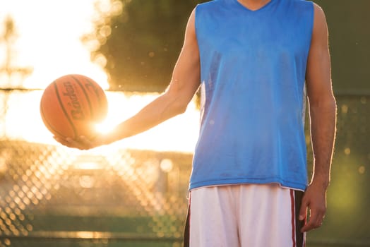 Athlete man holding basketball ball standing on playground at sunset