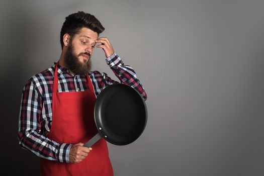 Man in red apron looking at frying pan and thinking what to do