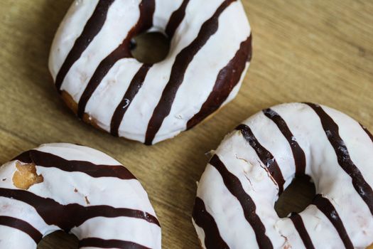 close up of vanilla donuts on table. The donuts have white glaze with brown chocolate