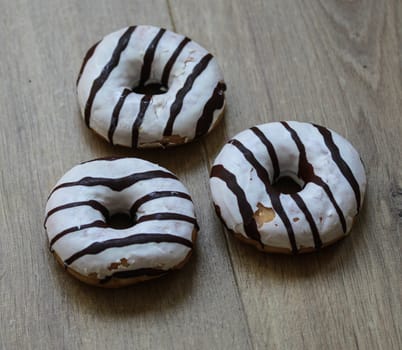 close up of vanilla donuts on table. The donuts have white glaze with brown chocolate