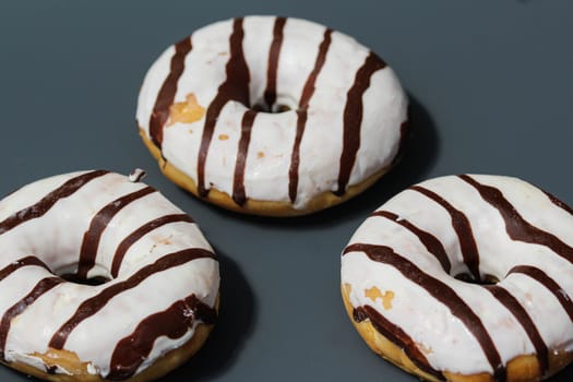 close up of vanilla donuts on table. The donuts have white glaze with brown chocolate