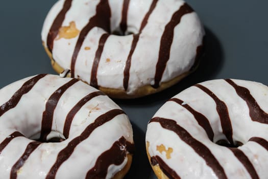 close up of vanilla donuts on table. The donuts have white glaze with brown chocolate