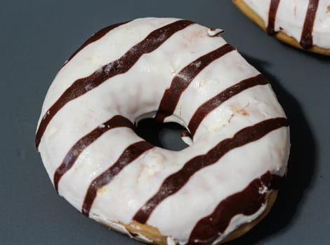 close up of vanilla donuts on table. The donuts have white glaze with brown chocolate