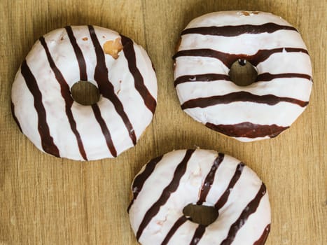 close up of vanilla donuts on table. The donuts have white glaze with brown chocolate