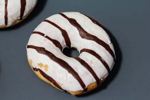 close up of vanilla donuts on table. The donuts have white glaze with brown chocolate