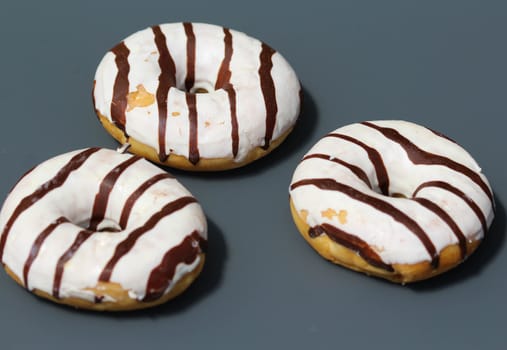 close up of vanilla donuts on table. The donuts have white glaze with brown chocolate