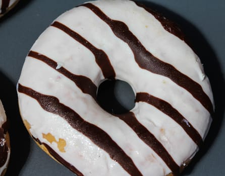 close up of vanilla donuts on table. The donuts have white glaze with brown chocolate