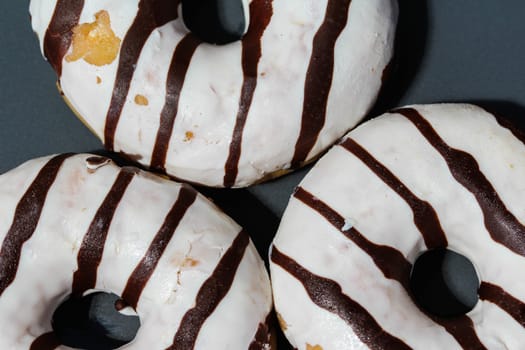 close up of vanilla donuts on table. The donuts have white glaze with brown chocolate