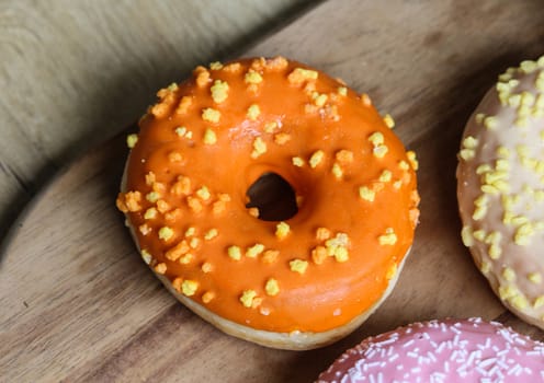 close up of a single orange donut with sprinkles on a wooden background
