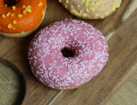 close up of a single strawberry donut with sprinkles on a wooden background