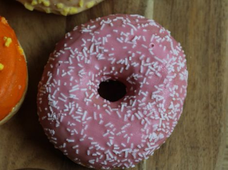 close up of a single strawberry donut with sprinkles on a wooden background