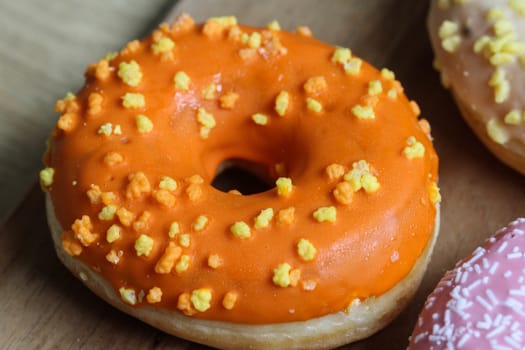 close up of a single orange donut with sprinkles on a wooden background