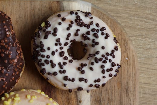 close up of vanilla donuts on table. The donuts have white glaze with brown chocolate