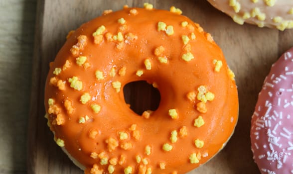 close up of a single orange donut with sprinkles on a wooden background