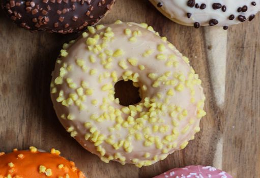 close up of a single strawberry donut with sprinkles on a wooden background