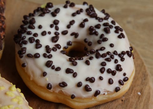 close up of vanilla donuts on table. The donuts have white glaze with brown chocolate