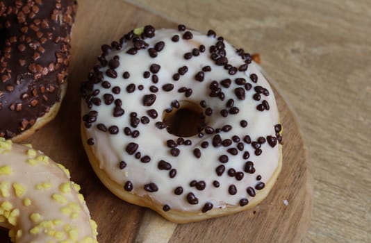 close up of vanilla donuts on table. The donuts have white glaze with brown chocolate