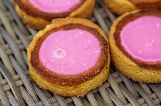 close up of Self made Dutch Butter Cake (Boterkoek) cookie with pink glaze, fresh baked from the oven. Displayed on wooden background. Made in the kitchen
