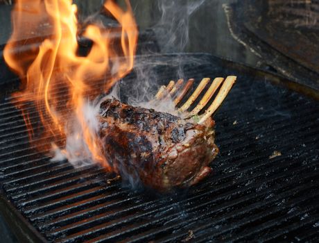 Rack of lamb on a barbecue. A flash of flame and cloud of smoke escapes from the grill around the meat.