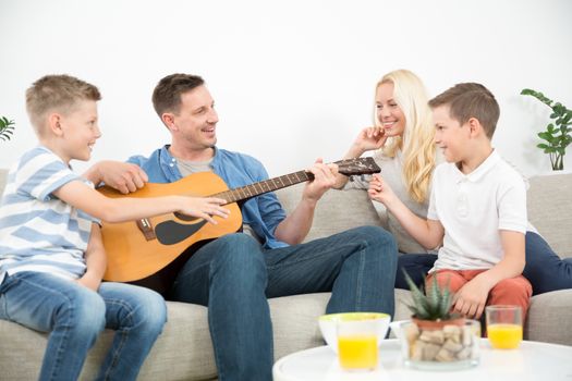 Happy caucasian family smiling while playing guitar and singing songs together at cosy modern home. Spending quality leisure time with children and family concept.