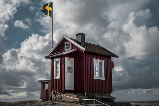 A classic Swedish red hut in front of a Swedish flag in the Gothenburg archipelago