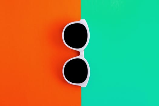 Sunny stylish white sunglasses on a bright blue-cyan and red-orange background, top view, isolated. Copy space. Flat lay.