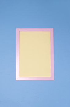 Empty pink photoframe with yellow paper inside on blue background. Copy space. Top view. Vertical. Minimal style concept.