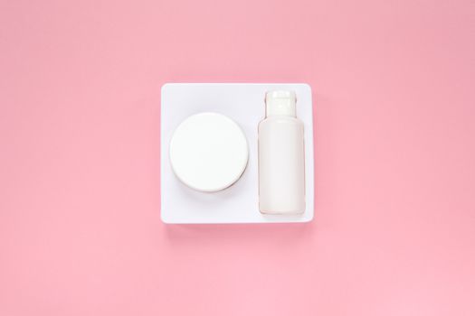 Home skin care system, cream and tonic in white packaging on pastel pink background, top view, flat lay. Beauty concept. Copy space