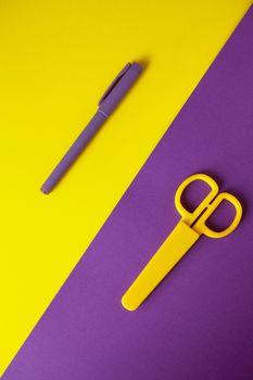 Yellow scissors on purple background, purple pen on yellow background. Diagonal composition. Back to school concept. Top view. Flat lay.