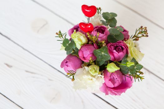 Creative flower bouquet on white wooden background. Focus on flowers, background is blurred. Copy space. For greeting card, social media, flower delivery, Mother's day, Women's Day