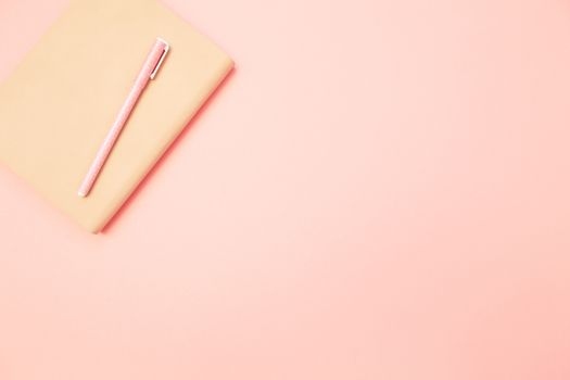 Beige diary with pink pen on pastel millennial pink paper background. Concept of education, blogging. Top view. Flat lay. Minimal style. Template for female blog. Lifestyle. Copy space.