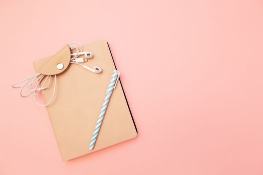 Beige diary with blue pen and headphones on pastel millennial pink paper background. Concept of education, blogging. Top view. Flat lay. Minimal style. Template for female blog. Lifestyle. Copy space.