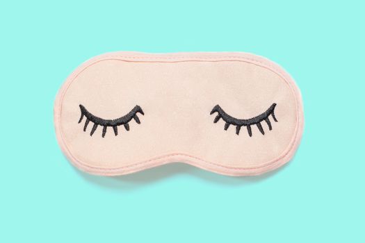 Pastel pink sleep mask with closed eyes embroidered on it with eyelashes on turquoise background. Top view, flat lay. Concept of vivid dreams. Accessories for girls and young women. Minimal style.