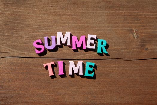 Inscription summertime by multicoloured wooden letters on wooden surface. Concept happy summertime.