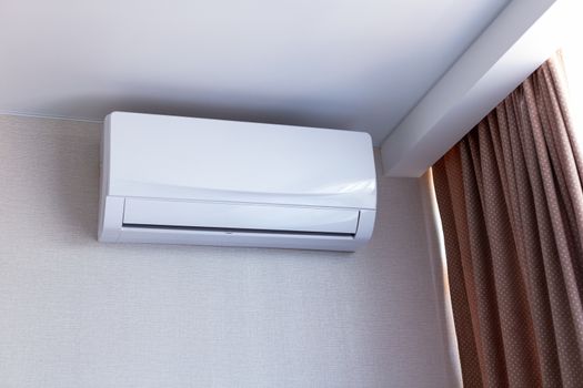 Small air conditioning on the wall inside room in apartment, switched off. Interior in calm beige tones.