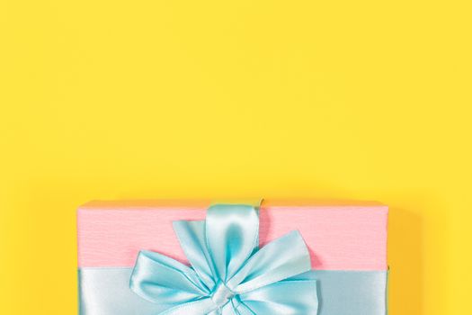 Pink gift box tied with blue ribbon with bow at the top on yellow background. Copy space for text. Minimal flat lay. Top view. Birthday, New year, Mother's day, Women's day celebration concept