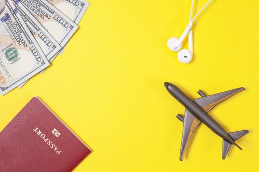 One hundred dollar bills, airplane, headphones, foreign passport on bright yellow paper background. Copy space. Travel and business concept, flat lay. Hand luggage, minimalism, frame of objects