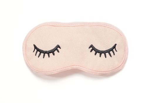 Pastel pink sleep mask with closed eyes embroidered on it with eyelashes on white background. Top view, flat lay. Concept of vivid dreams. Accessories for girls and young women