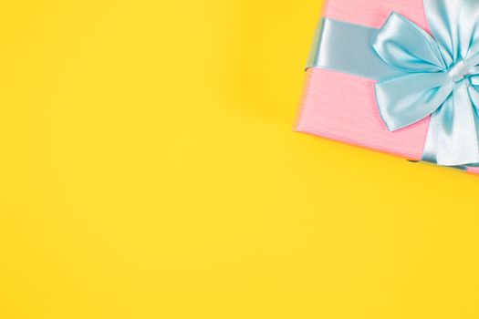Pink gift box tied with blue ribbon with bow at the top on yellow background. Copy space for text. Minimal flat lay. Top view. Birthday, New year, Mother's day, Women's day celebration concept