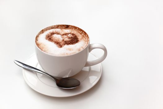 Cappuccino cup on white table background. Foam is decorated with cinnamon heart. Copy space. Top view, located at side of frame. Horizontal. Mock up for social media, food blog, lifestyle. Soft focus.