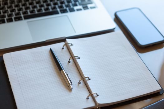 Working space, top view. Laptop, mobile phone and open notebook with pen on beige desktop. Notepad sheets on silver brackets, automatic ballpoint pen in silver-black colour. Business background