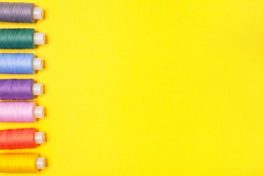Handicraft background. Set of multicolored spools of thread on yellow background with copy space. Accessories for needlework, embroidery, sewing. Flat lay. Top view. Objects are lined up on left side.