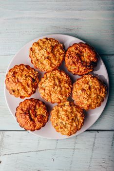 Cooked oatmeal muffins on white plate over light wooden background. View from above.