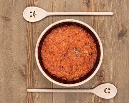 A ceramic pot of traditional Eastern European stewed cabbage and decorated wooden spoons on a brown wooden kitchen board.