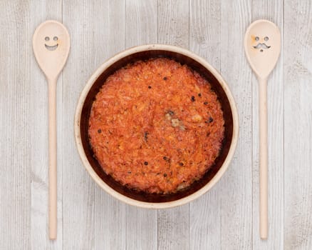 A ceramic pot of traditional Eastern European stewed cabbage and decorated wooden spoons on a white wooden kitchen board.