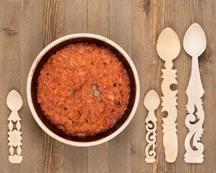 A ceramic pot of traditional Eastern European stewed cabbage and decorated wooden spoons on a brown wooden kitchen board.