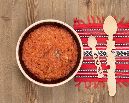 A ceramic pot of traditional Eastern European stewed cabbage and decorated table rug and wooden spoons on a brown wooden kitchen board.